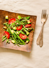 Fresh light green salad with avocado and tomatoes in a wooden plate. Top view.