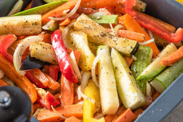 Chopped raw vegetables with spices for a vegetarian casserole in a baking dish close up - potatoes, peppers, tomatoes, onions, garlic, eggplants, zucchini