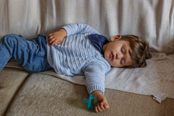 A tender little toddler boy dressed in blue, is resting peacefully on the sofa in his living room © Óscar