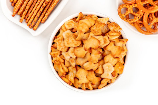 A closeup photo of salty fish crackers, sticks, and pretzels, shot from above on a white background with copy space. Party snacks mix with a place for text
