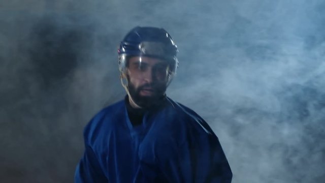 Professional hockey player with a stick and a puck moves on Luda in skates and helmet on a dark background and smoke. Dribbling with the puck of a young man on the ice arena
