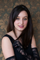 Fototapeta premium Medium vertical portrait of gorgeous smiling brunette young woman in sleeveless dress wearing high lace gloves, sparkling headband and necklace