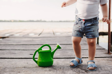 A small girl is playing with a watering can of a wooden bridge. Spring and summer. Gardening. green watering can