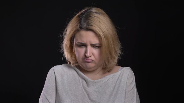 Blonde short-haired overweight business woman blowing up cheeks watching downwards sadly on black background.