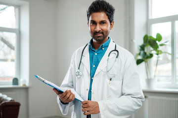 Indian doctor with stethoscope around neck in his office