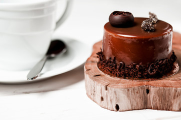 A delicious chocolate cake with chocolate pieces lies on a wooden stand next to a white cup, which stands on a white table