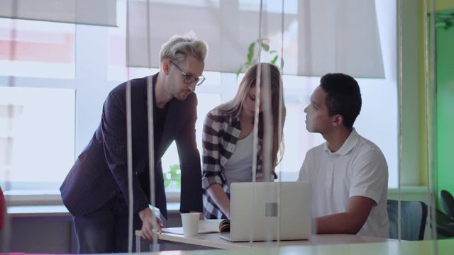 Zoom in of young diverse business team of three discussing strategy at office. Young man listening to team leader while woman taking notes.