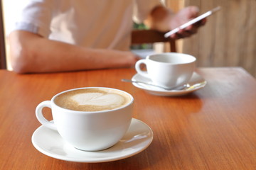 Businessman using social media by mobile phone in the cafe with the cup of latte coffee on the table with copy space