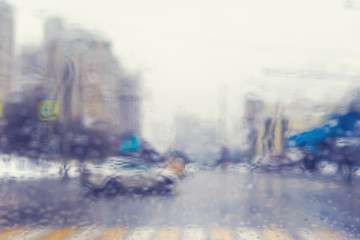 Blurred view through the windshield of a car with raindrops at a crossroad and pedestrian crossing.