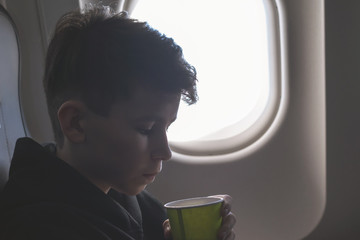 A boy have flight looking in the airplane window or porthole.