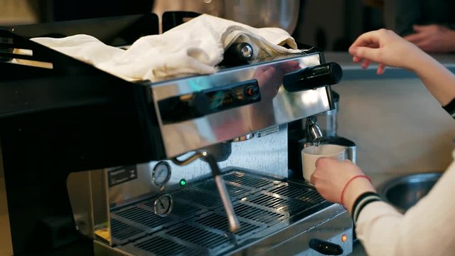 The girl fills a cup with hot water from the coffee machine. Hands close up. Hand girl baristas dub coffee from holder coffee machines