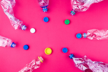 Crushed plastic bottles and colorful caps on vivid pink purple background.