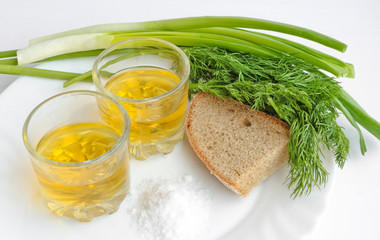 Pepper vodka in two transparent glasses, green onions, dill, rye bread and coarse salt - still life.