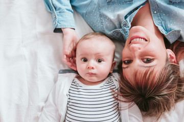 happy young mother and her baby boy lying on bed and smiling