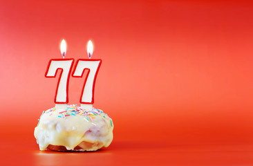 Seventy seven years birthday. Cupcake with white burning candle in the form of number 77. Vivid red background with copy space