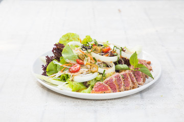 Close up of rare seared tuna slices with fresh vegetable salad on a plate with wood background