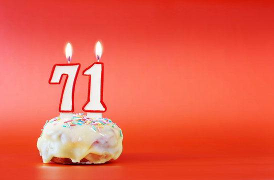 Seventy one years birthday. Cupcake with white burning candle in the form of number 71. Vivid red background with copy space