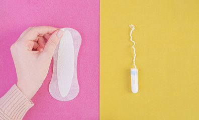 Hygiene care during critical days. Choosing between a tampon and a sanitary pad. Menstrual cycle. The woman holds in hands of a sanitary pad. Top view