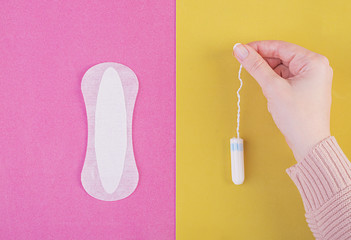 Hygiene care during critical days. Choosing between a tampon and a sanitary pad. Menstrual cycle. The woman holds in hands of a tampon. Top view