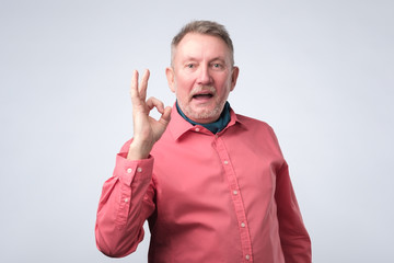Senior european man in red shirt showing OK sign