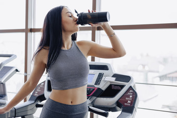Fototapeta na wymiar Girl in the gym are trained on treadmill and drink water