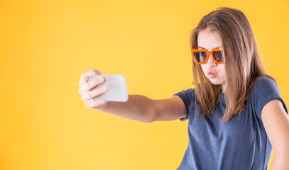 Portrait of crazy teen girl with retro glasses making selfie over yellow background