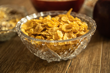 Corn flakes in a crystal bowl, fresh red organic apple and other healthy food on wooden table