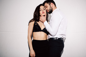 handsome man touching face of sexy woman in black bra standing on white