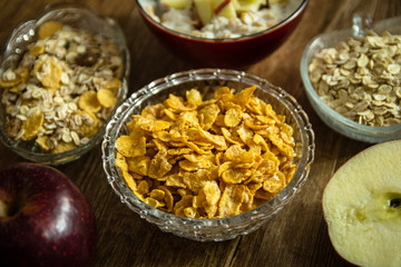 Corn flakes in a crystal bowl, fresh red organic apple and other healthy food on wooden table