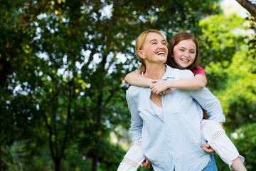 Fototapeta premium Small happy girl enjoying a piggyback ride on her mothers back