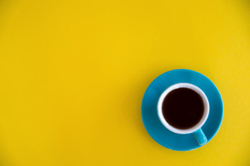 Blue cup of coffee stands on a yellow background. Morning breakfast, business.
