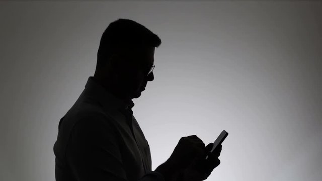 Silhouette of a man on a white background. A man writes a message in the phone. Woman uses the internet in a smartphone.