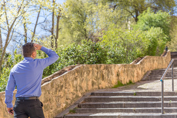 Fototapeta premium An elegant man in a blue shirt looks attentively on a street uphill with stairs
