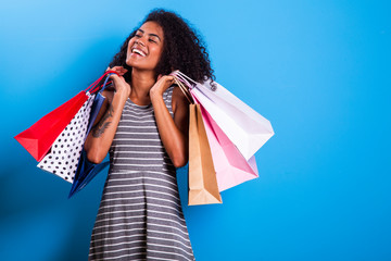 Young black woman holding shopping bags on blue backgrond.