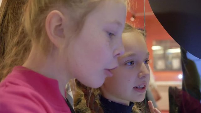 Two girl teenagers using interactive screen to buy tickets in modern metro station. Young teenager girl watching interactive screen in museum of modern art. Happy face young girl