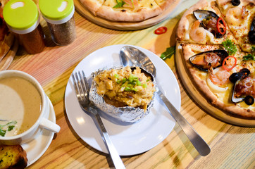 Woman eating baked mash potato wrap with aluminium foil. Lunch, dinner at restaurant
