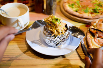 Woman eating baked mash potato wrap with aluminium foil. Lunch, dinner at restaurant
