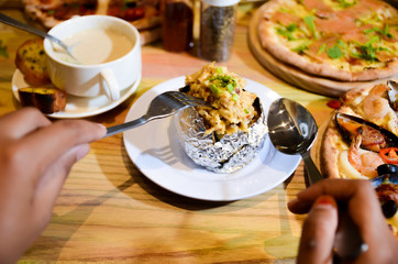Woman eating baked mash potato wrap with aluminium foil. Lunch, dinner at restaurant