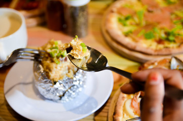 Woman eating baked mash potato wrap with aluminium foil. Lunch, dinner at restaurant