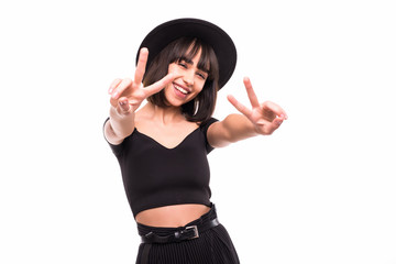 Close-up portrait of pretty hipster girl in black hat showing peace gesture and looking at camera on white background