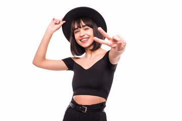 Close-up portrait of pretty hipster girl in black hat showing peace gesture and looking at camera on white background