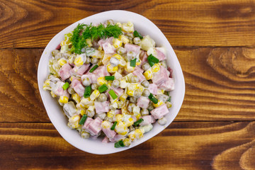 Tasty salad with sausage, green pea, canned corn, bell pepper, cucumber and mayonnaise on wooden table. Top view