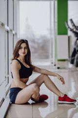 Relaxing after training. Top view of beautiful young woman looking away while sitting on the floor at gym