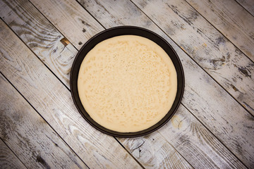 Round pizza dough is in the pan. The process of cooking pizza, stacking ingredients on the dough.