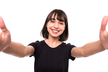 Smiling young woman in glasses casualy dressed taking a selfie with outsretched hands standing isolated over white background