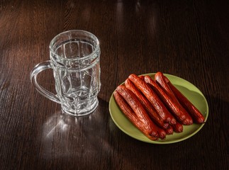 An empty beer glass and smoked sausage on the table.