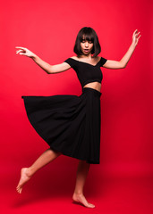 Naklejka premium Beautiful woman in black flying dress isolated on red background