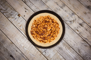 Round pizza dough is in the pan. The process of cooking pizza, stacking ingredients on the dough.