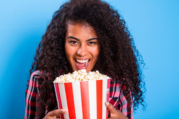 African american woman eating popcorn happy with big smile on blue background