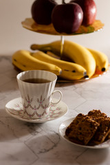apples and bananas with a cup of tea and cookies on a light background